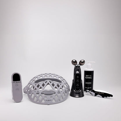 A skincare set on a light gray background, including a gray mesh head, a black facial cleansing device, a black bottle labeled SKIN ACID KINSE, a black spatula, and a gray remote control.